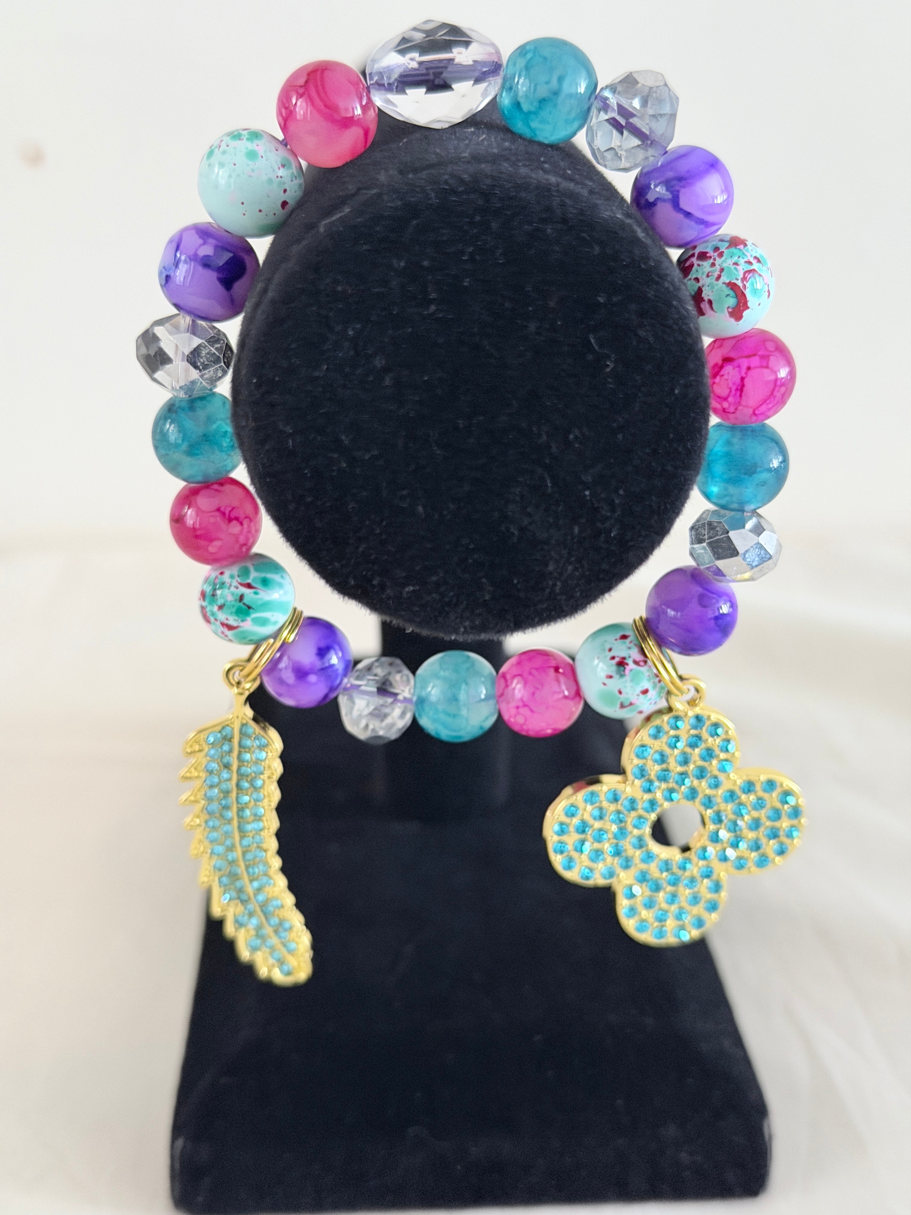 Multicolour mixed bead bracelet with gold turquoise rhinestone flower and feather charms on black jewellery stand - LoyatobsCreations.com