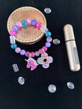 Pink and teal marbled bead bracelet with silver rhinestone unicorn and multicolour flower charms flat lay on dark background - LoyatobsCreations.com