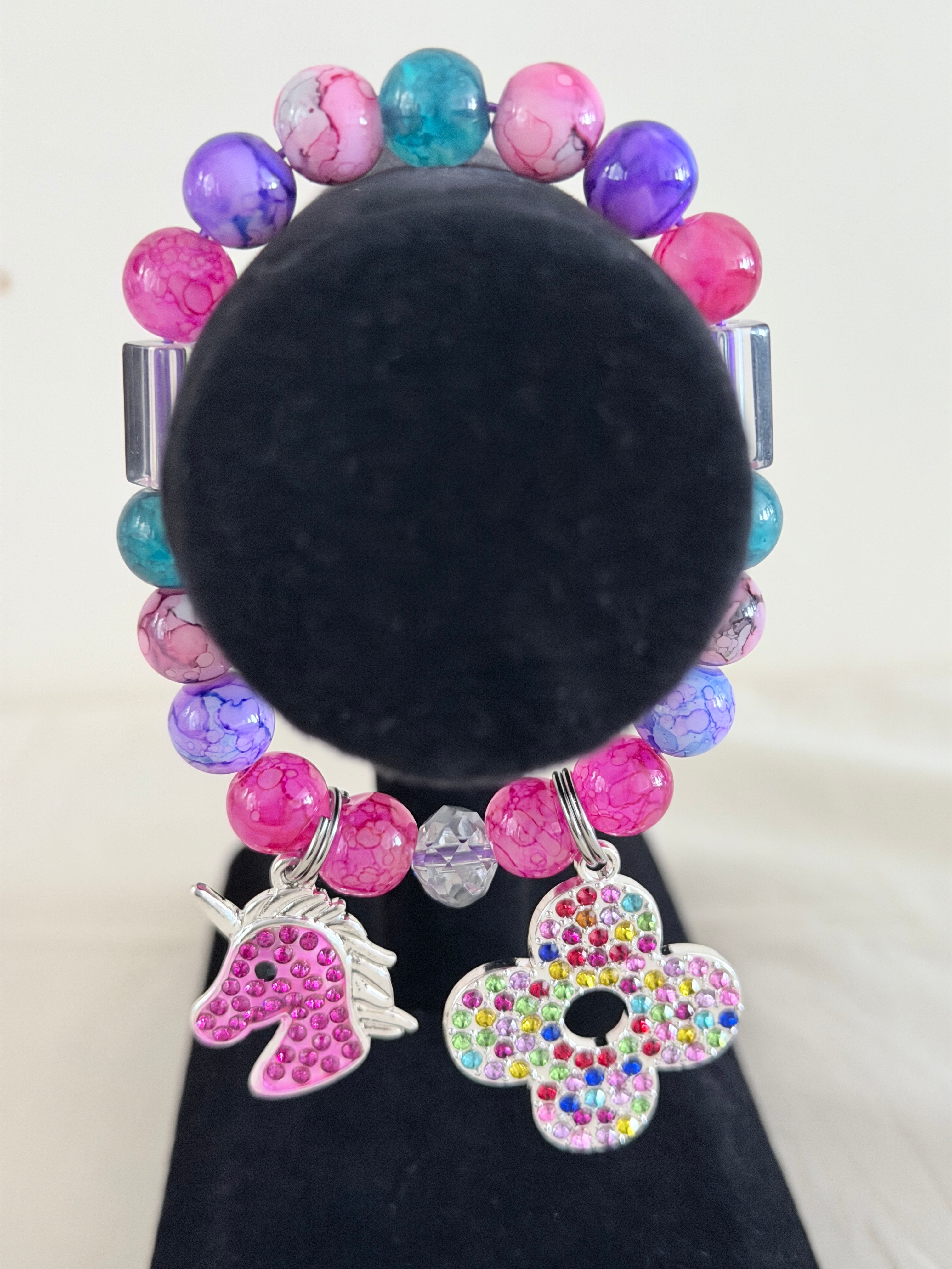 Pink and teal marbled bead bracelet with silver rhinestone unicorn and multicolour flower charms on black jewellery stand - LoyatobsCreations.com