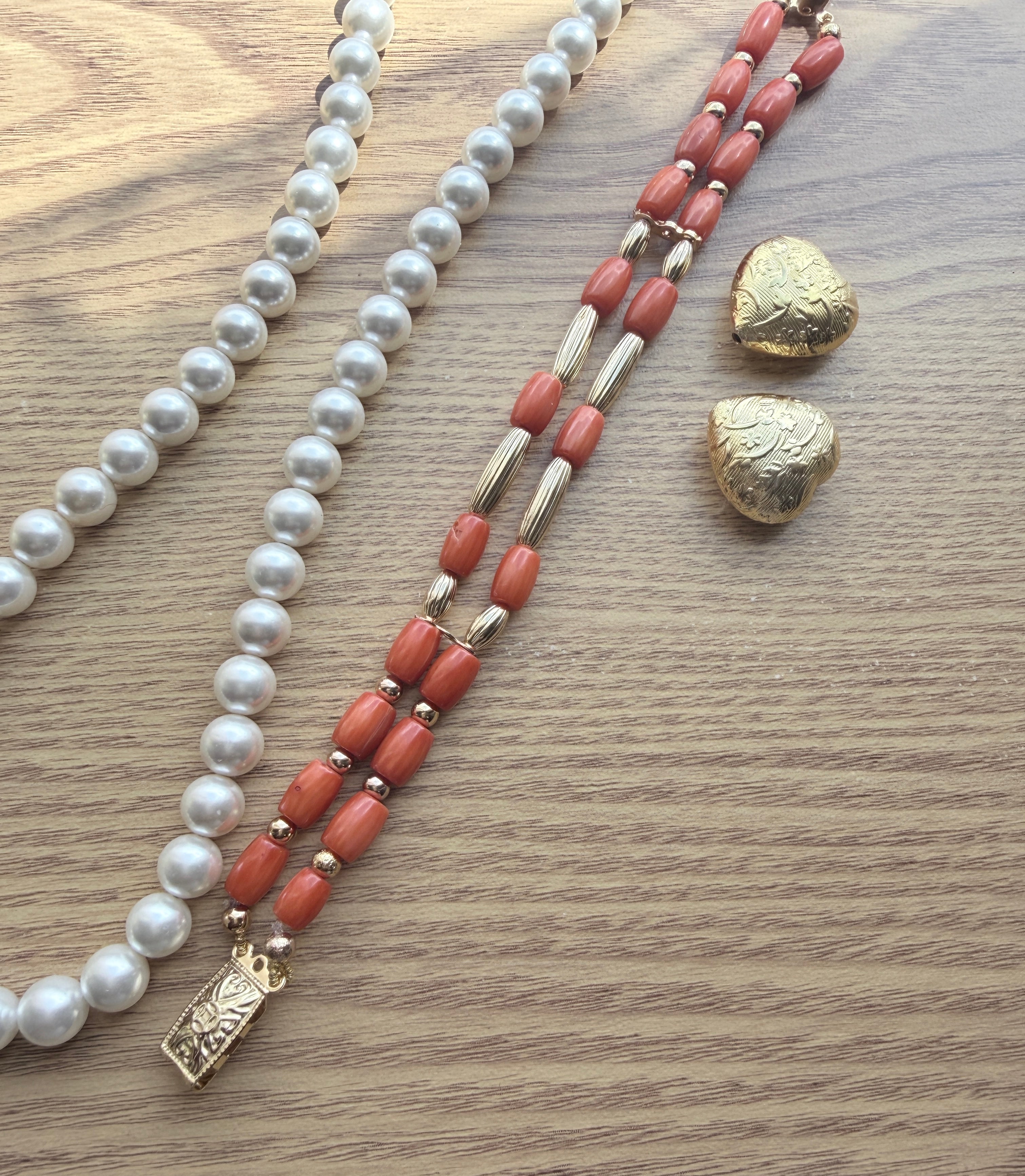 "Lifestyle shot of coral tube two-row bracelet styled with pearl necklace and gold heart accessories on wood surface"