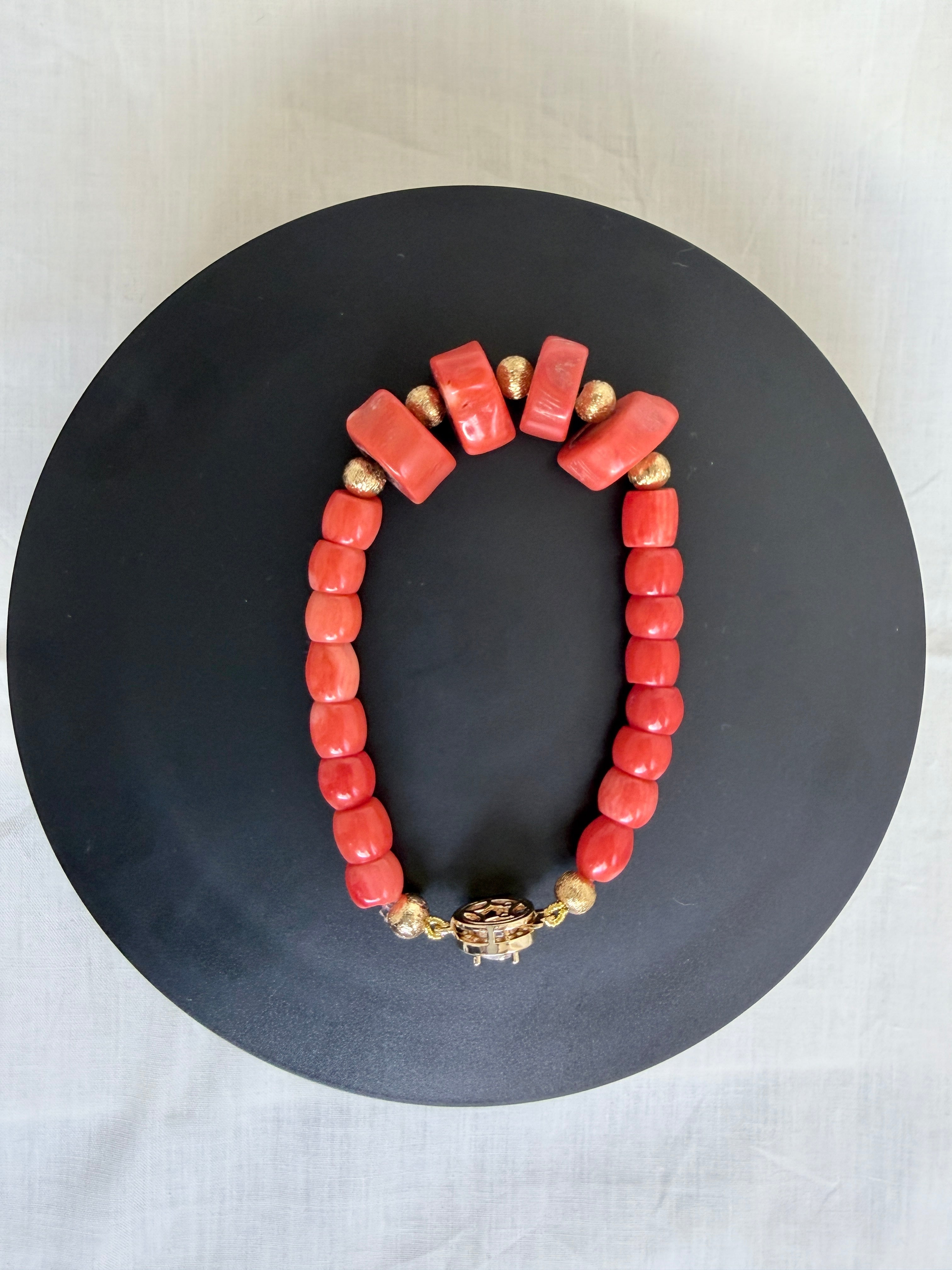 "Coral barrel bracelet with CZ clasp laid flat on a black circle board showing full bracelet shape and decorative gold fish hook clasp"