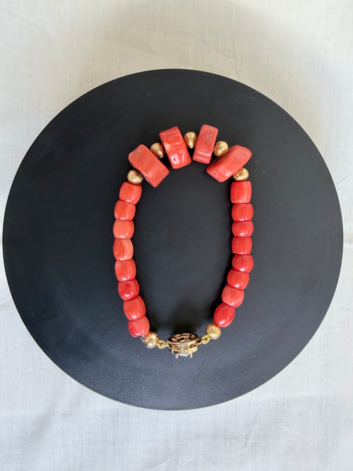 "Coral barrel bracelet with CZ clasp laid flat on a black circle board showing full bracelet shape and decorative gold fish hook clasp"