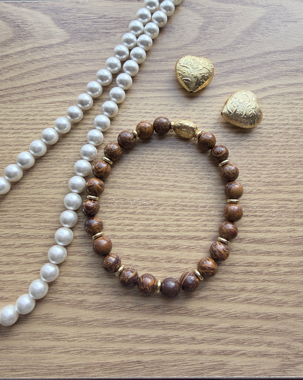 "Lifestyle shot of elephant skin jasper bracelet styled with pearl necklace and gold heart accessories on wood surface"