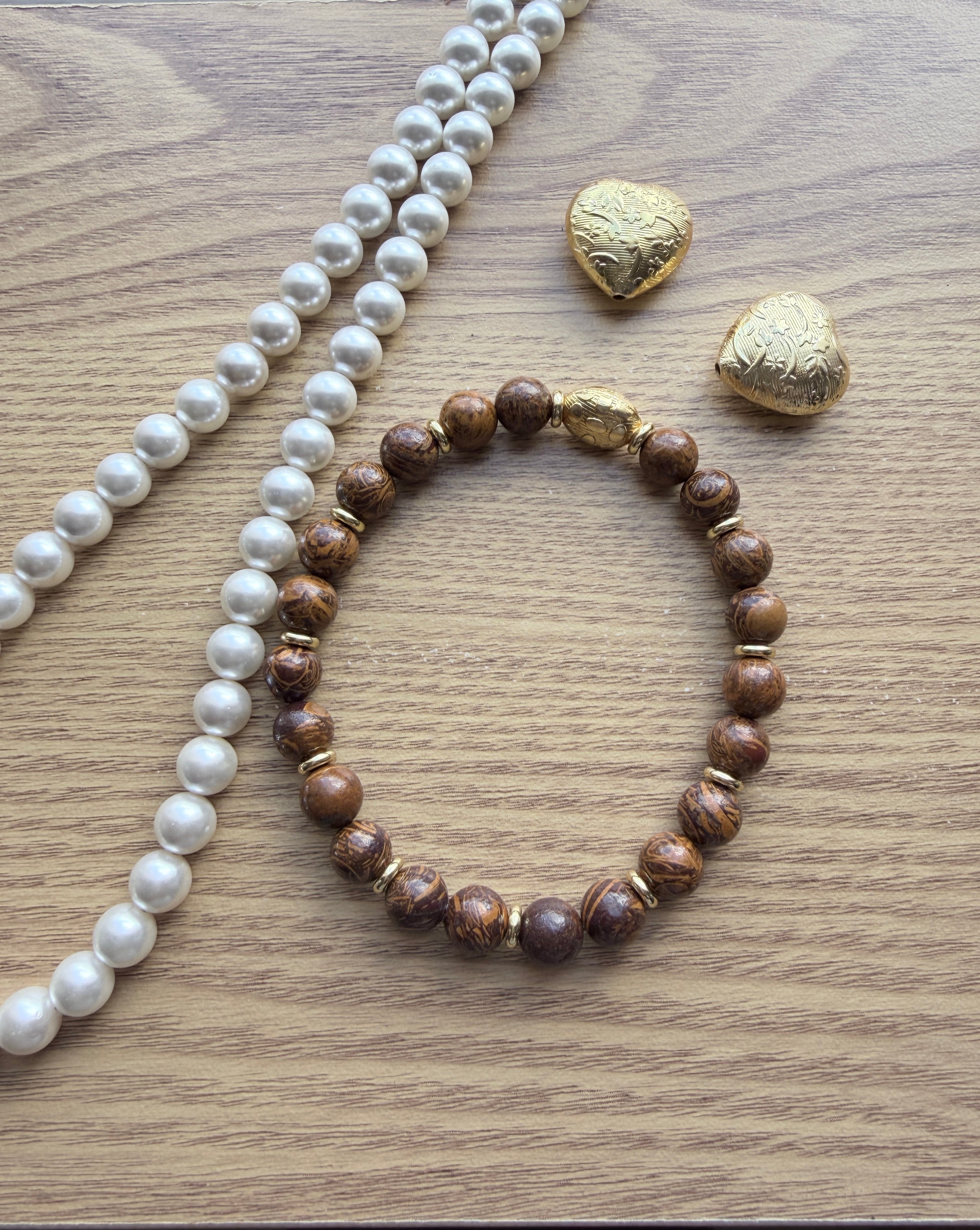 "Lifestyle shot of elephant skin jasper bracelet styled with pearl necklace and gold heart accessories on wood surface"