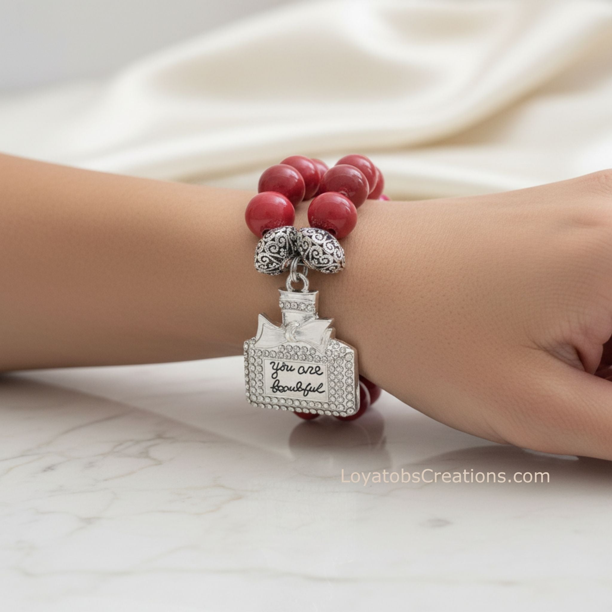 Coral ceramic bead bracelet with silver rhinestone You Are Beautiful perfume bottle charm worn on wrist on marble background - LoyatobsCreations.com
