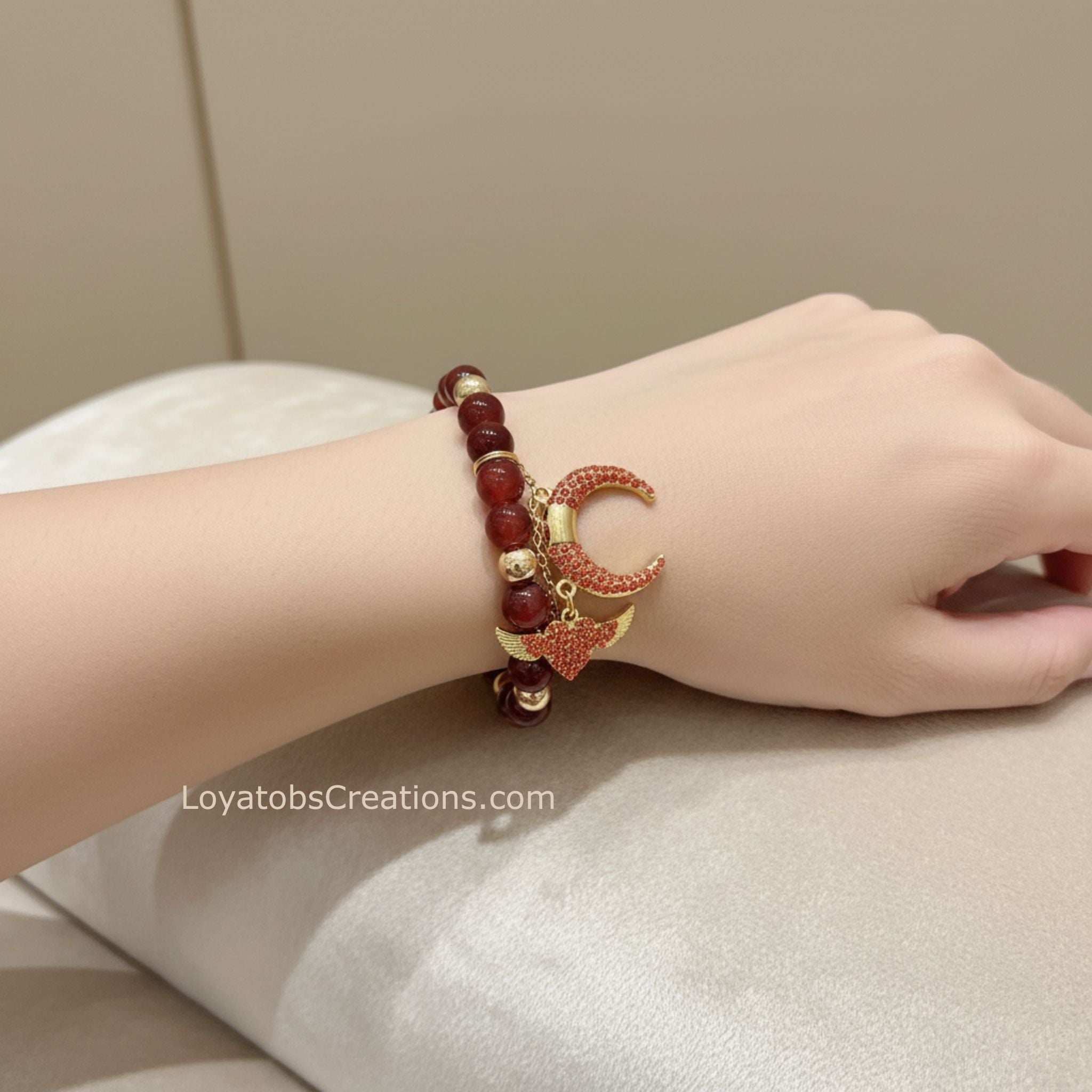 Burgundy ceramic bead bracelet with gold rhinestone crescent moon and winged heart charms worn on wrist - LoyatobsCreations.com