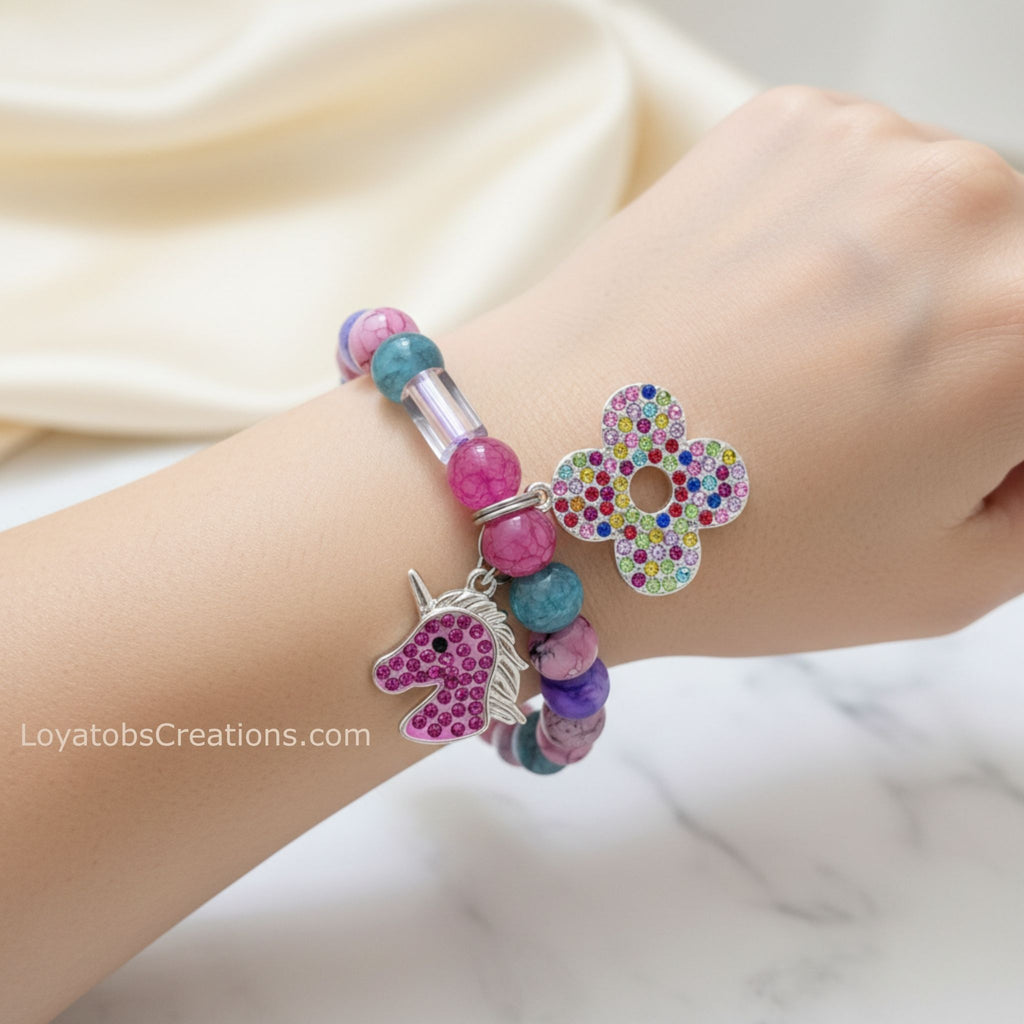 Pink and teal marbled bead bracelet with silver rhinestone unicorn and multicolour flower charms worn on wrist on marble background - LoyatobsCreations.com