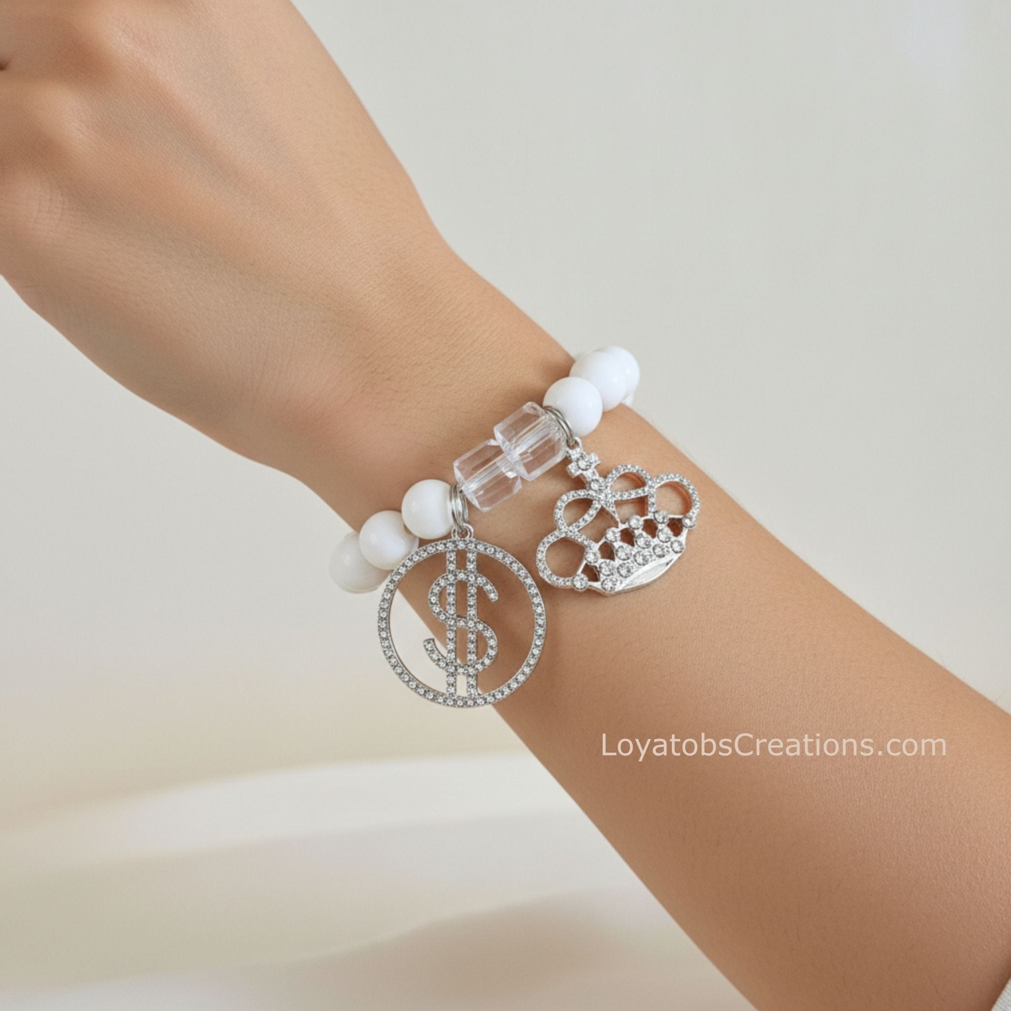 White bead and crystal cube bracelet with silver pavé dollar sign and crown charms worn on wrist - LoyatobsCreations.com